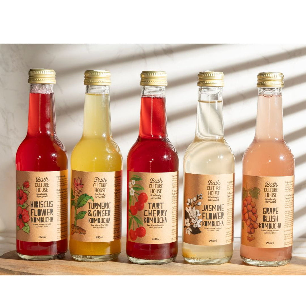 Five bottles of Bath Culture House kombucha on a wooden surface with a neutral background