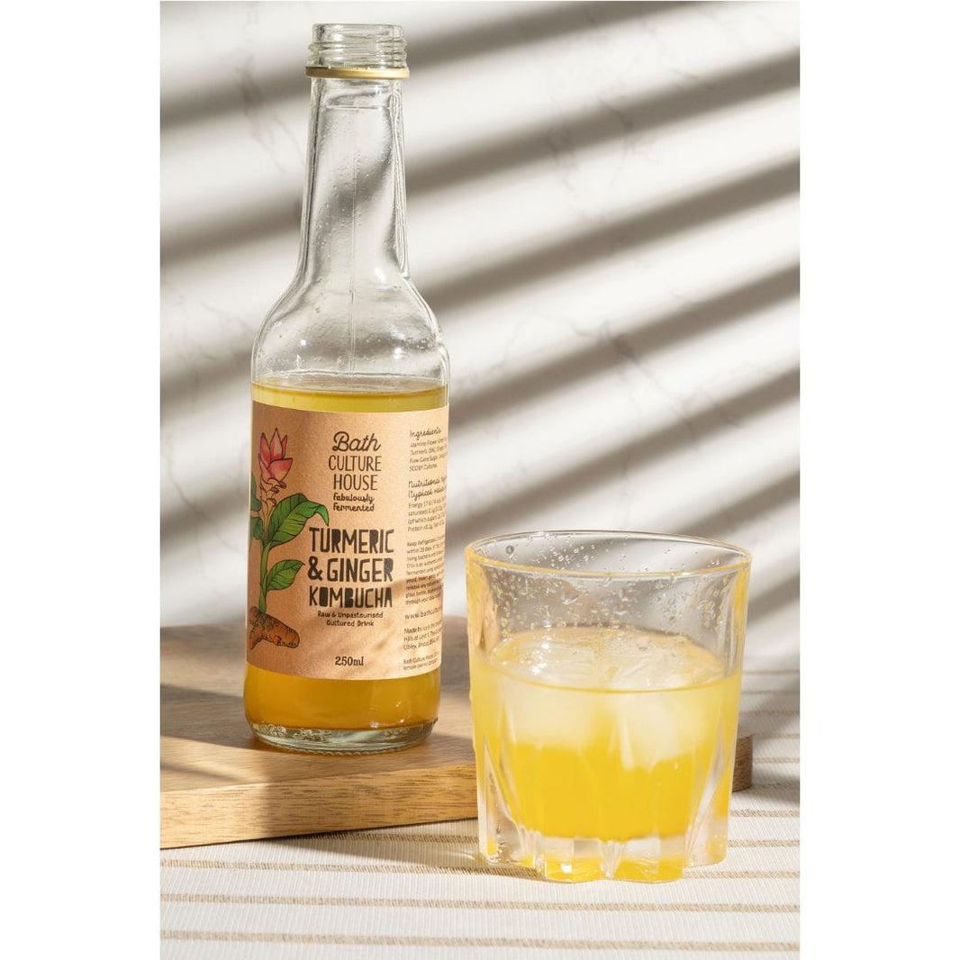 image Bottle of Bath Culture House Turmeric & Ginger Kimchi with a glass of the drink on a striped surface.