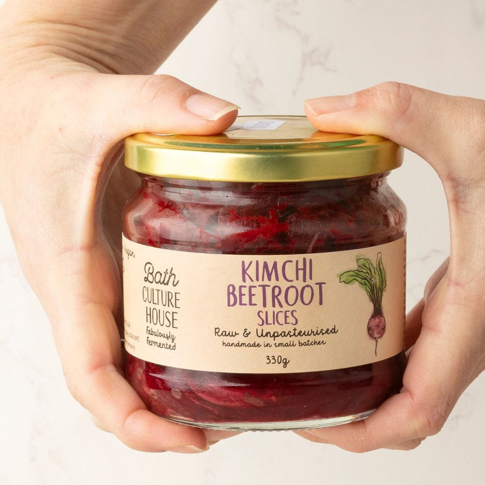 Jar of Kimchi Beetroot Slices held by two hands with a neutral background