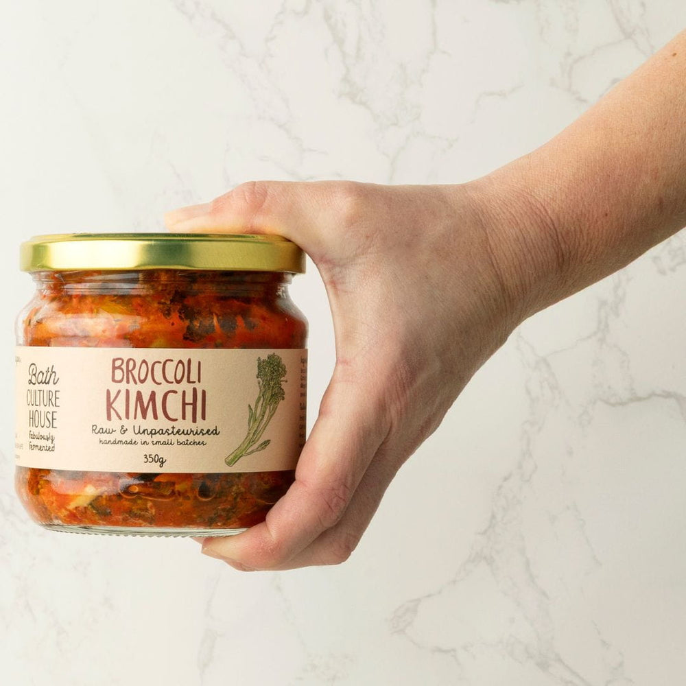 Hand holding a jar of Broccoli Kimchi with a visible label on a light background