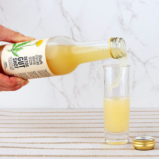 Bottle of 'Bath Culture House' Detox Gut Shot being poured into a glass on a white background.