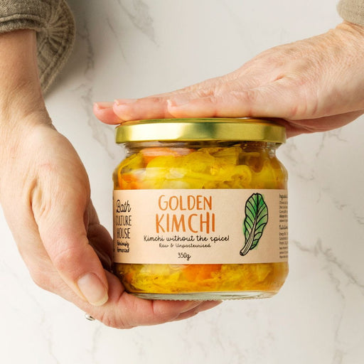 Jar of Golden Kimchi held by a person on a marble surface