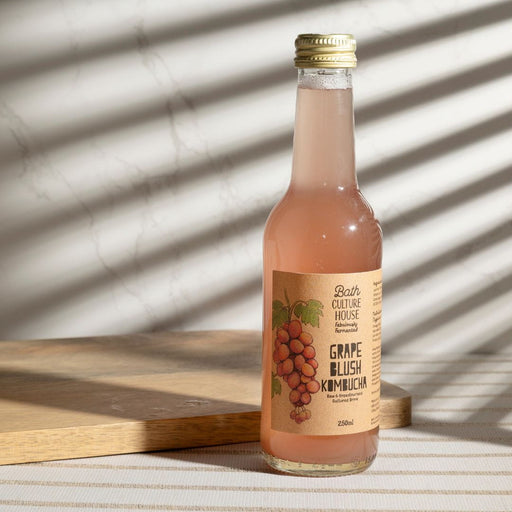 Bottle of Grape Blush Kombucha on a wooden surface with a striped background