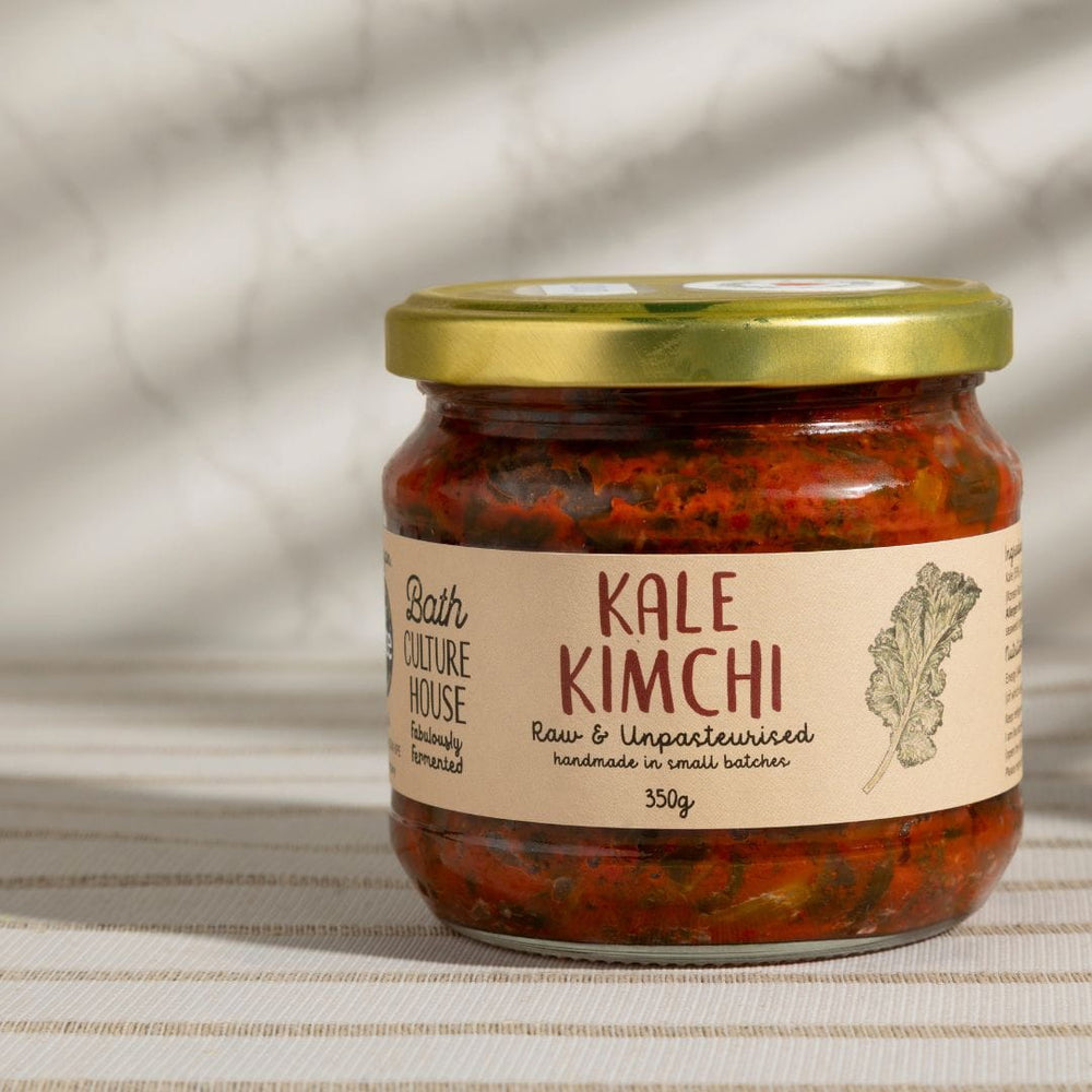 Jar of Kale Kimchi with a gold lid on a textured surface