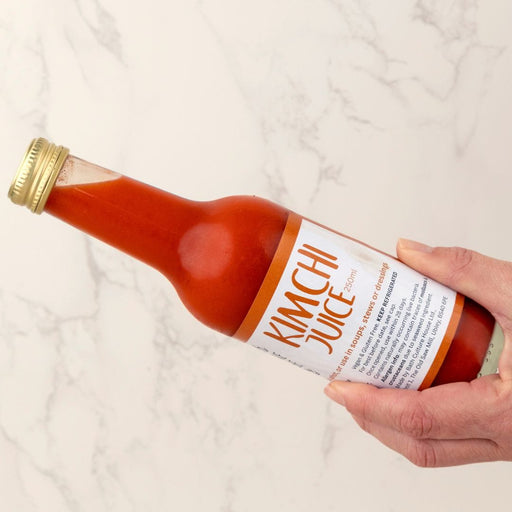 Bottle of kimchi juice held by a hand on a white background