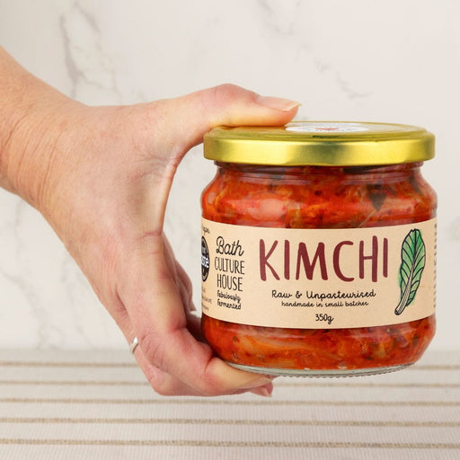 Hand holding a jar of kimchi with a visible label on a neutral background