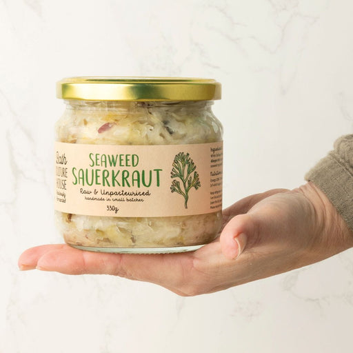 Hand holding a jar of seaweed sauerkraut with a visible label on a white background