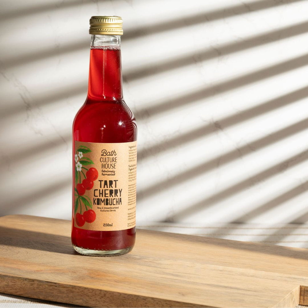 Bottle of Tart Cherry Kombucha on a wooden surface with a light background