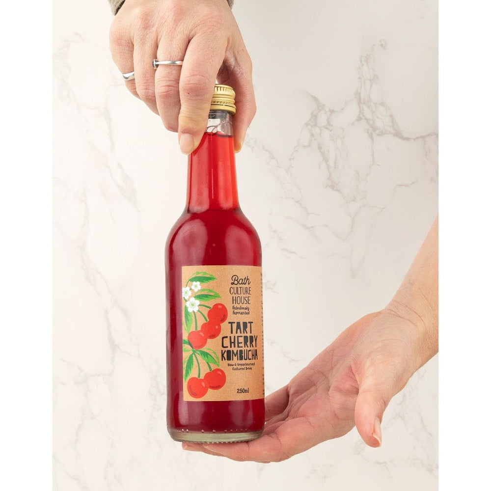 Bottle of tart cherry kombucha held by a person on a light marble background