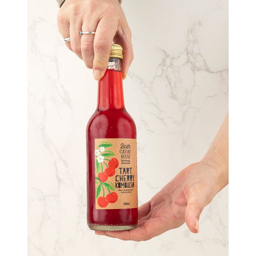 Bottle of tart cherry kombucha held by a person on a light marble background